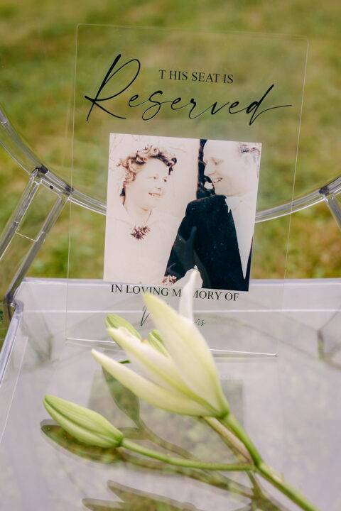 Pamiątkowe miejsce podczas ceremonii ślubnej z fotografią bliskich, napisem In loving memory of i białymi liliami